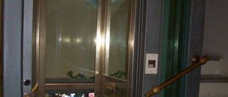 An elevator with a glass door, a metallic handle, and a visible emergency button.