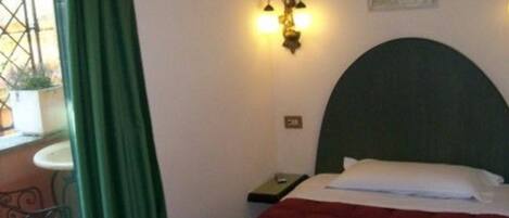 A hotel room with a bed, a nightstand, a wall-mounted light fixture, and a window with a curtain.