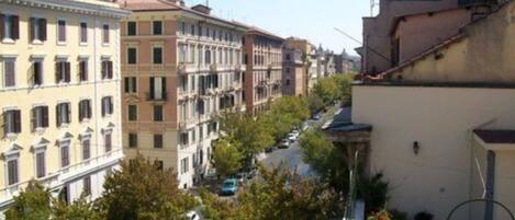 A street view with multi-story buildings, parked cars, and trees.