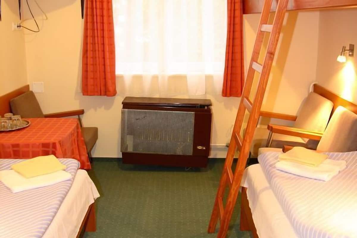 A hotel room with bunk beds, a small table with a chair, a television on a shelf, and a heater.