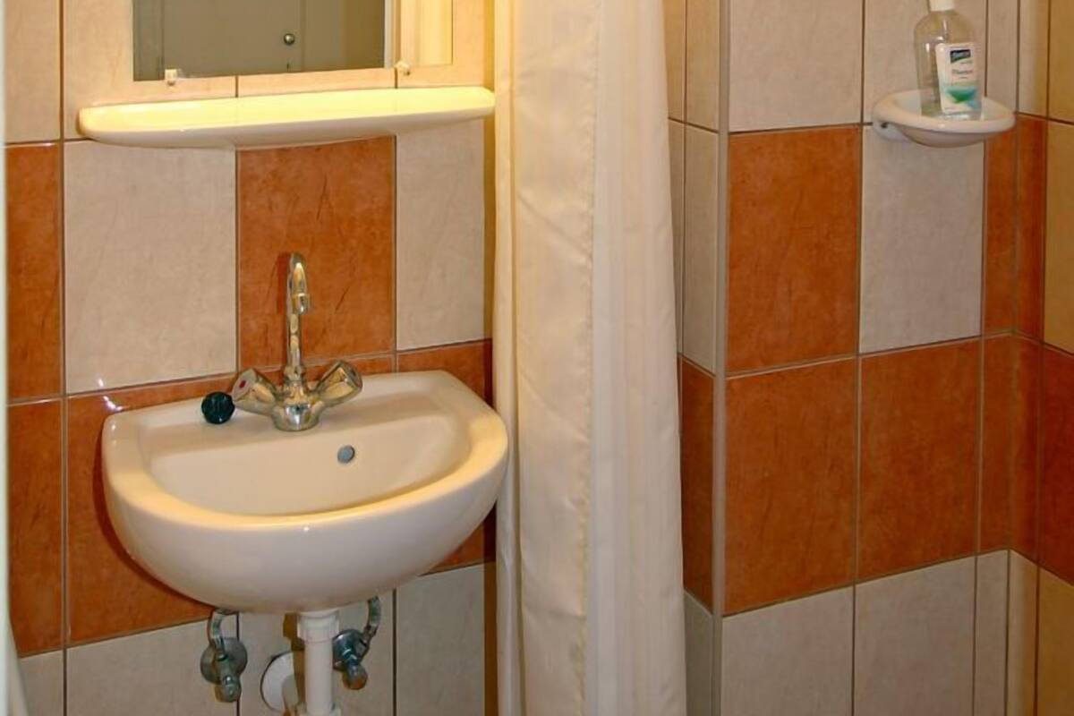 A bathroom with a sink, mirror, and a shelf with a bottle.