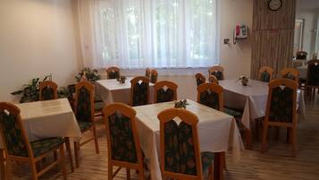 A dining area with multiple tables and chairs, a window with sheer curtains, a wall-mounted phone, and a radiator.