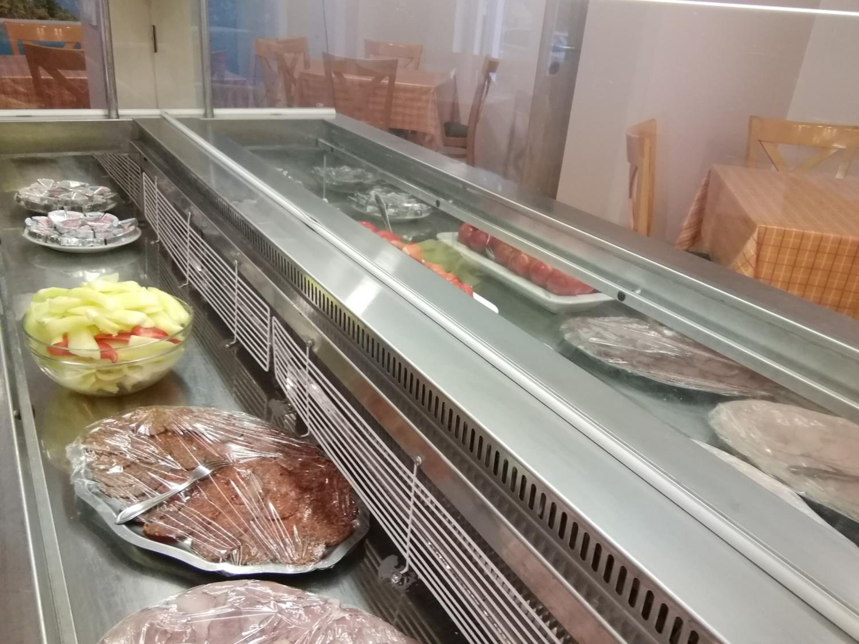 A deli counter with various food items, including sliced apples, wrapped sandwiches, and trays of meat.