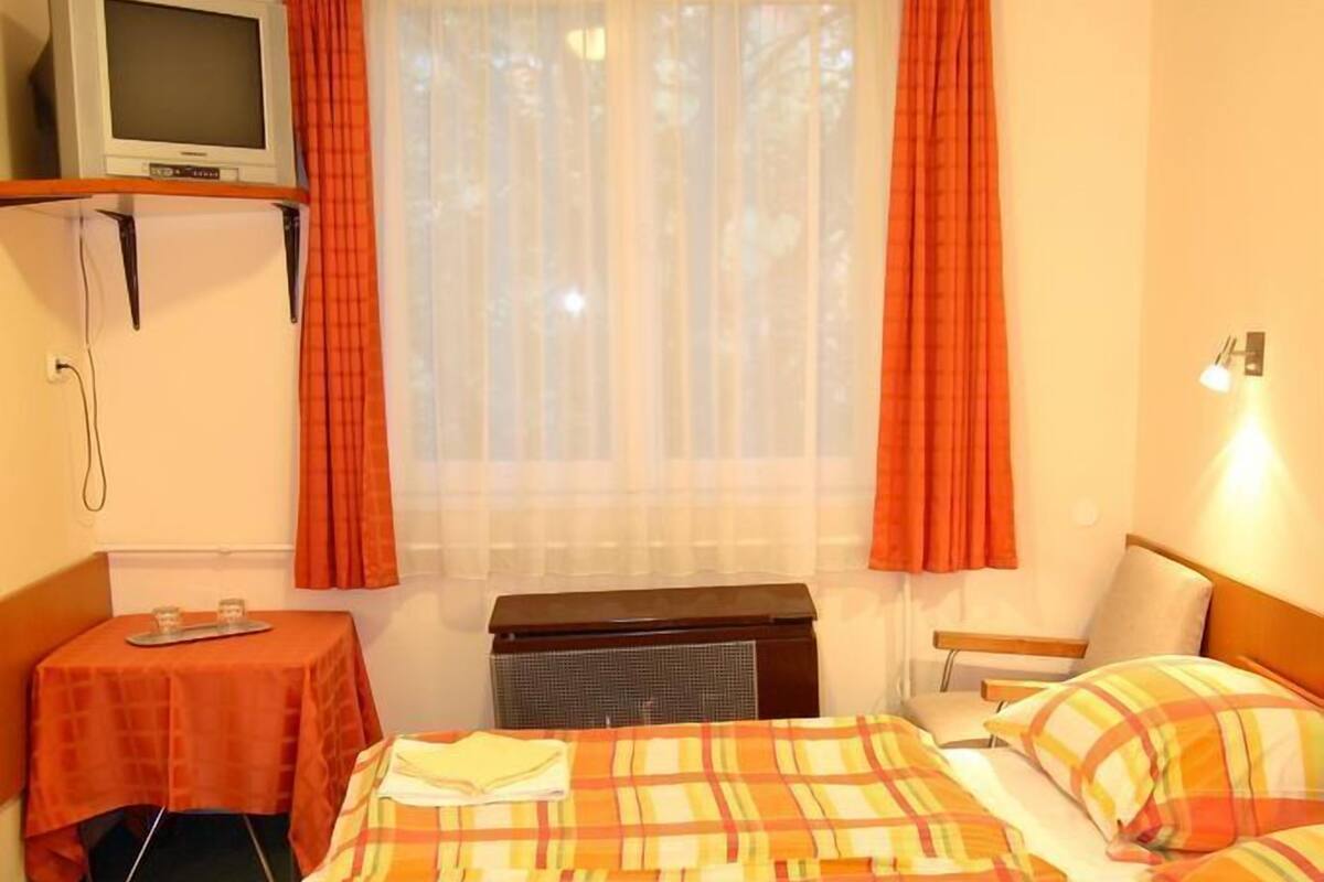 A hotel room with two beds, a television, a table, and a window with curtains.