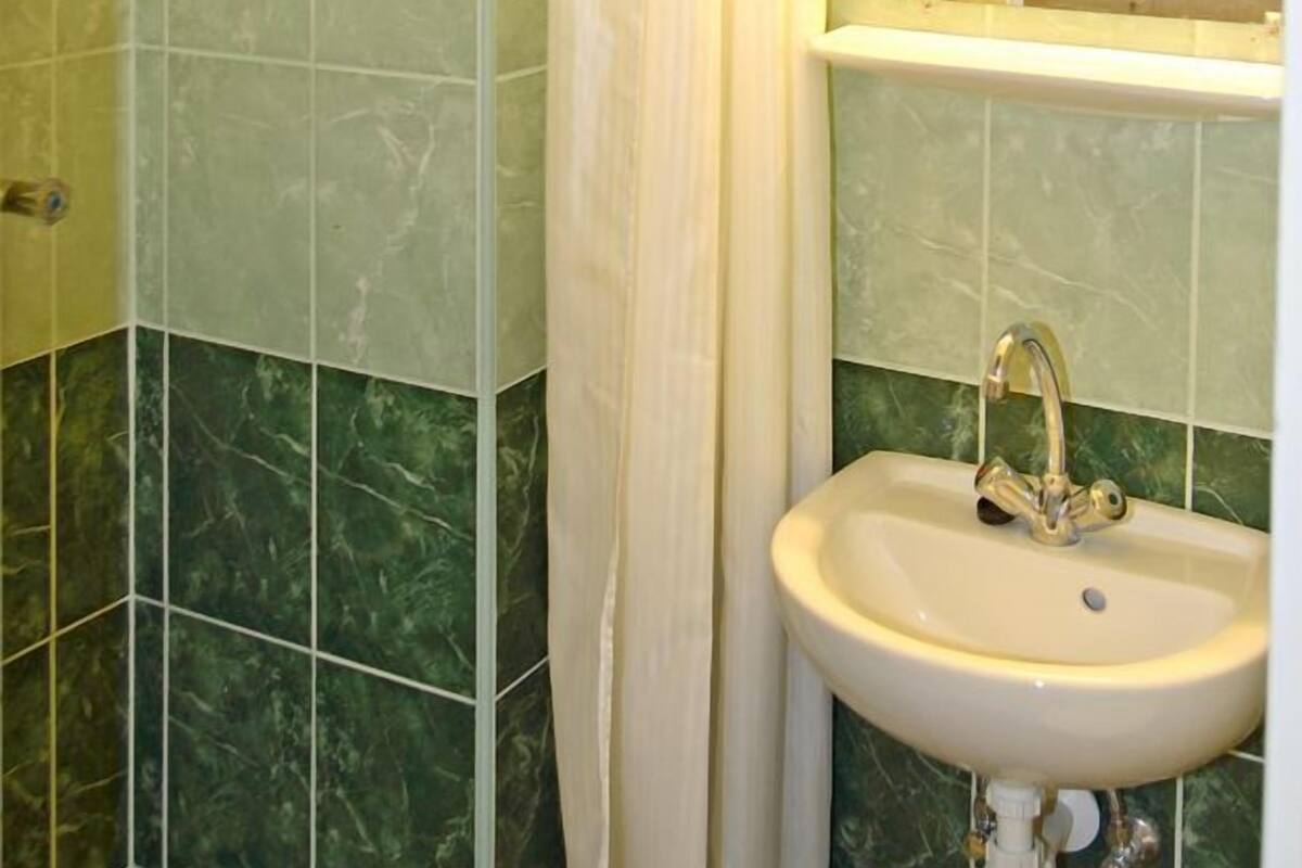 A bathroom with green marble tiles, a shower with a white curtain, and a sink with a mirror above it.