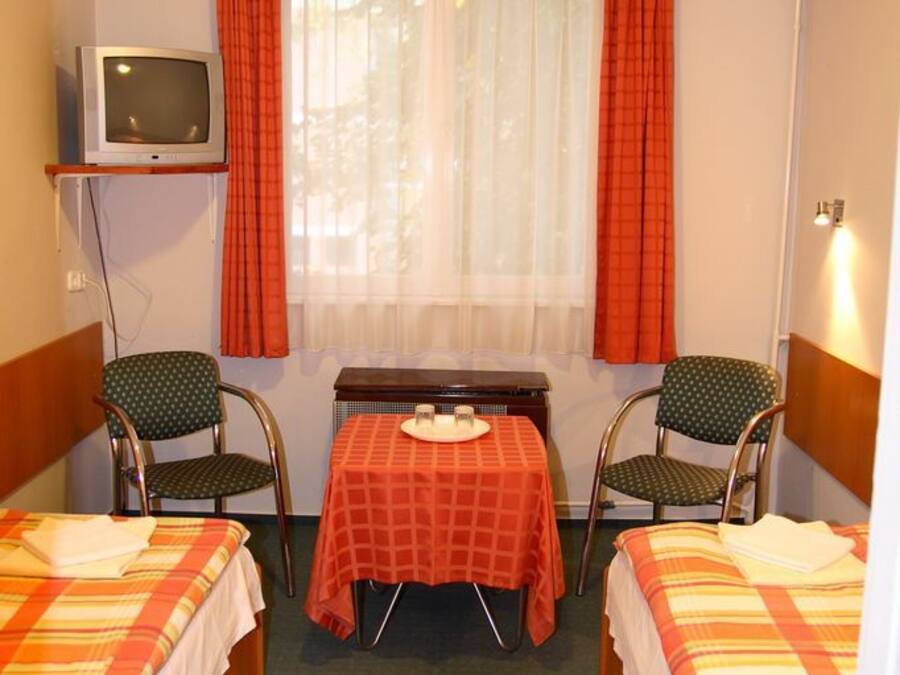 Una habitación de hotel pequeña con dos camas, una mesa, sillas, televisión y una ventana con cortinas.