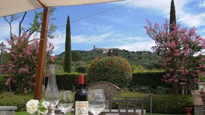Une table à manger installée à l’extérieur, agrémentée de verres à vin, d’une bouteille et d’assiettes, et entourée d’une végétation luxuriante et d’arbres en fleurs.