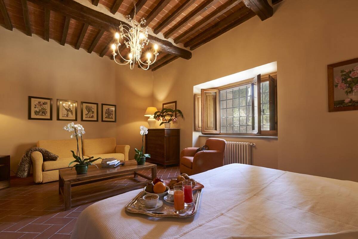 Een gezellige kamer met een bed, een bank, een bijzettafeltje met ontbijtartikelen, een kroonluchter en een raam met uitzicht.