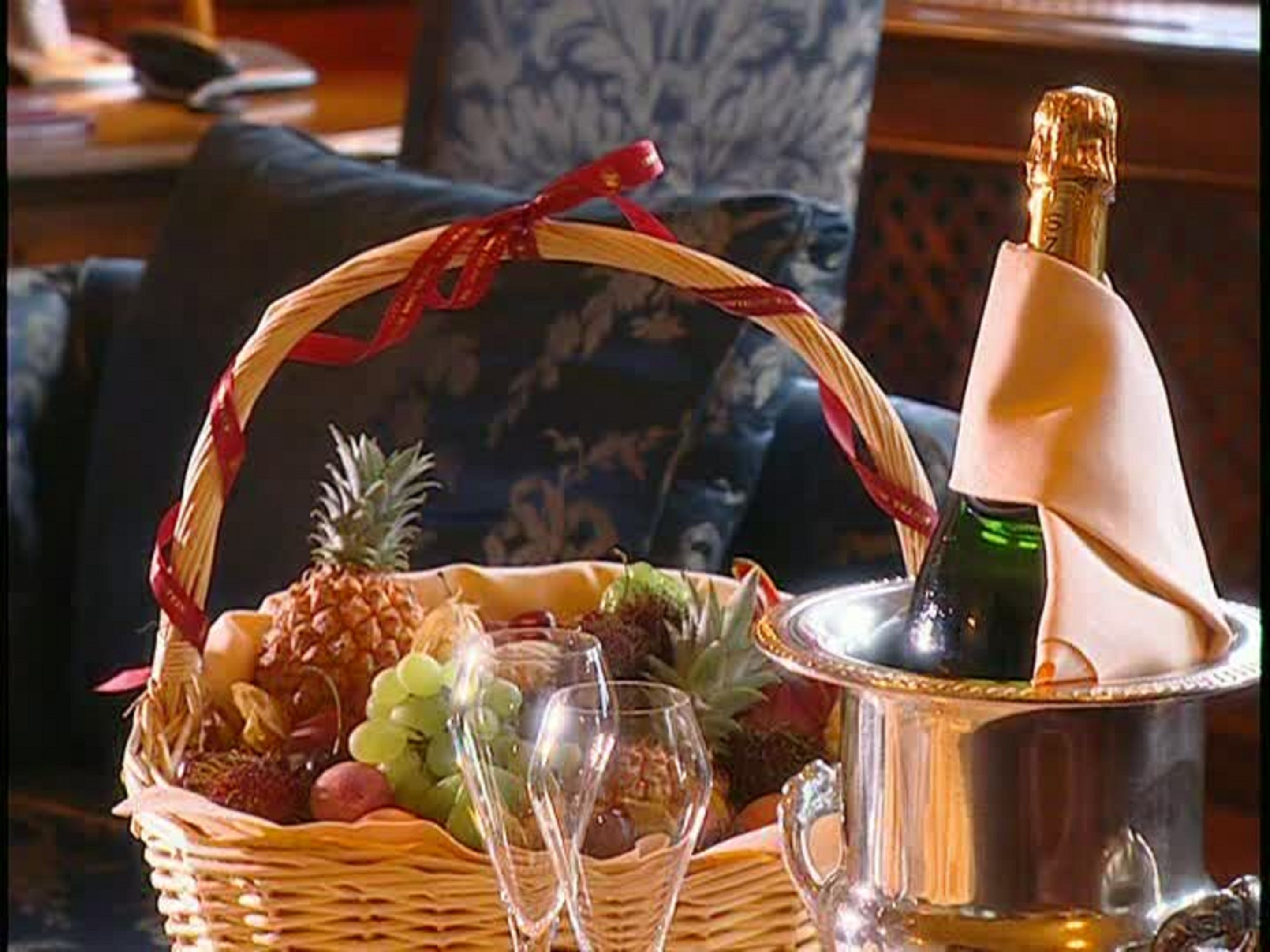A wicker basket filled with fruits and grapes, a bottle of champagne, and two champagne flutes on a table.