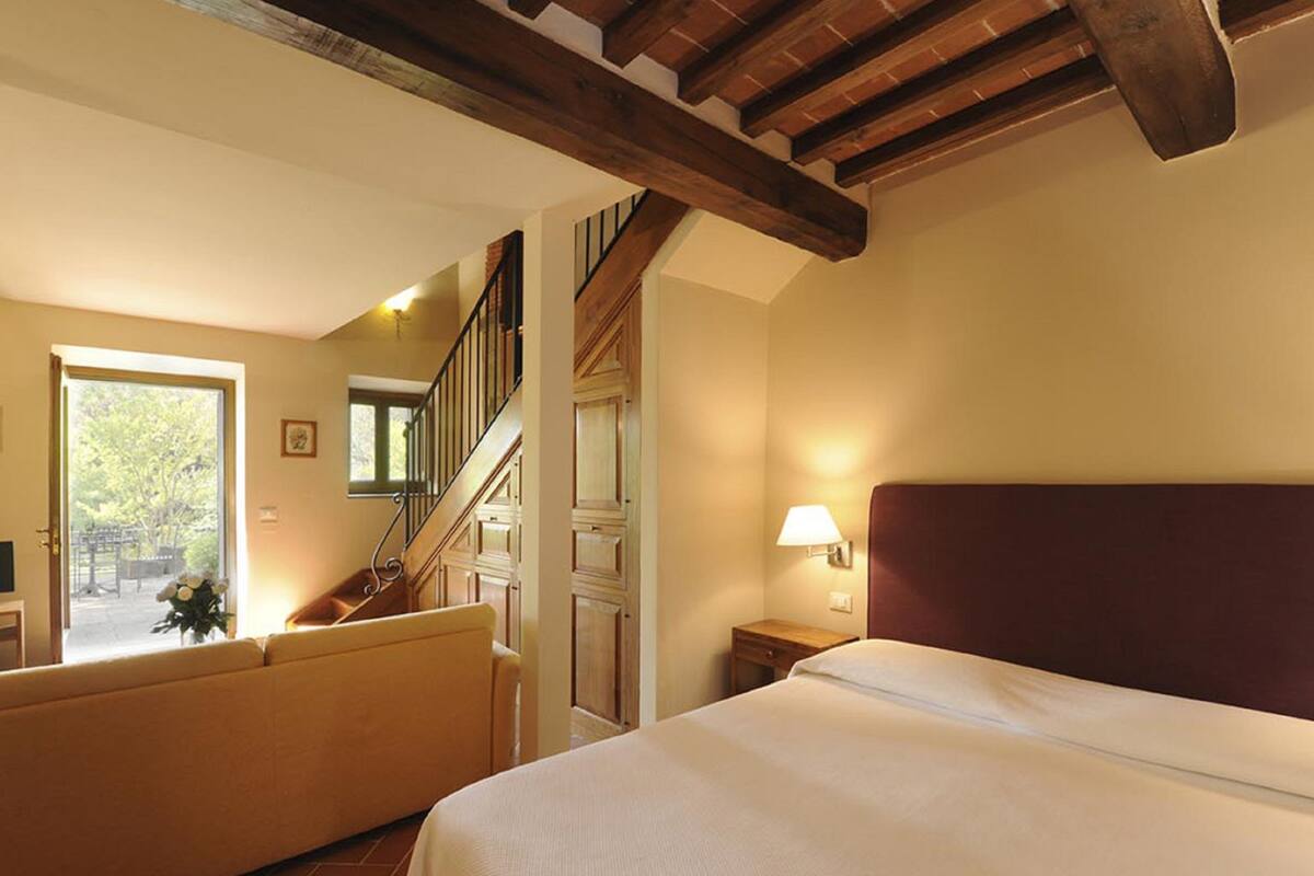 Een slaapkamer met een bed, nachtkastje, lamp, raam en een trap.