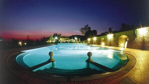 Une piscine au crépuscule, avec des murs en pierre et des éclairages.