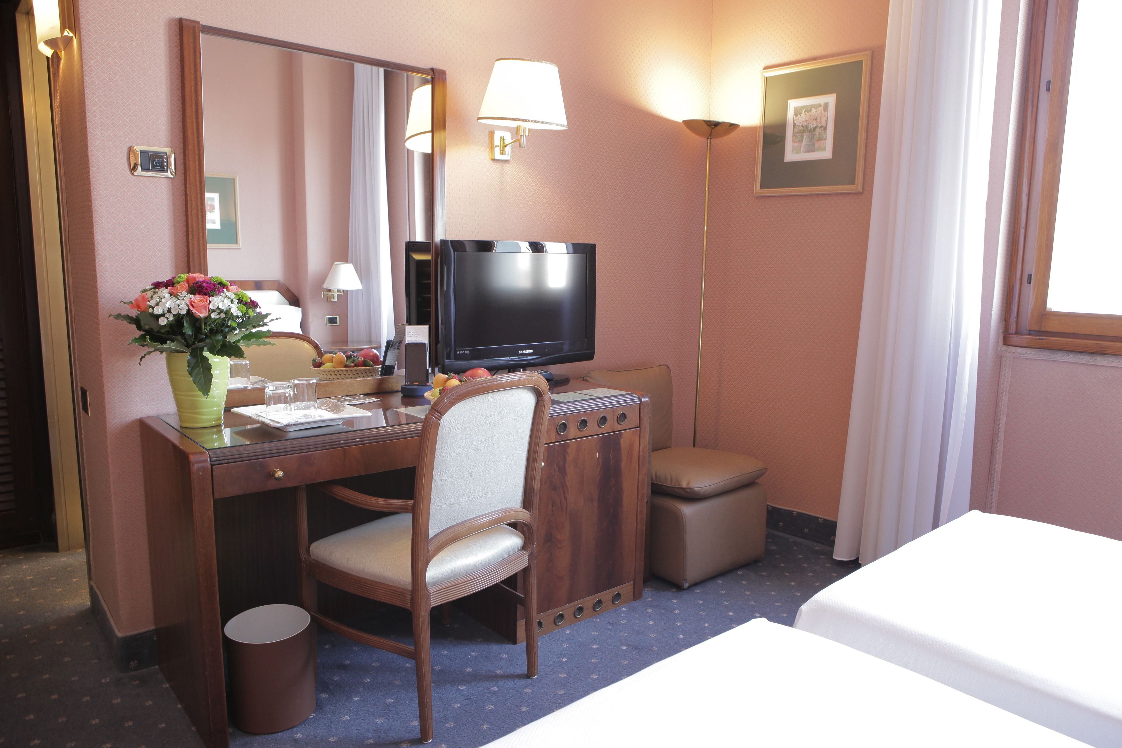 Una habitación de hotel con escritorio, silla, televisor, mesita de noche y cama.
