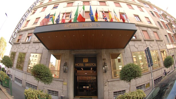 A hotel entrance with multiple flags, a prominent sign, and a classic architectural style. - Hotel Bristol (Milan)