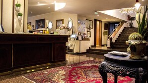 A hotel lobby with a reception desk, a staircase, and a decorative table with a cactus. - Hotel Bristol (Milan)