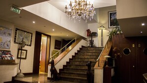 A grand staircase with a chandelier, a dog statue, and a wooden door with circular windows. - Hotel Bristol (Milan)