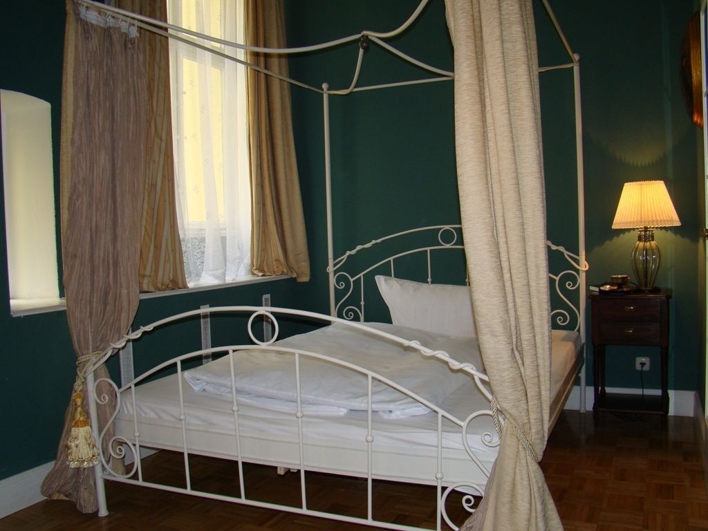 Una cama con dosel y estructura metálica blanca, junto a una mesita de noche con lámpara.