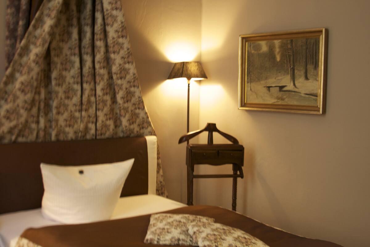 Une chambre d’hôtel avec un lit, une lampe, un tableau et un porte-manteau.
