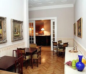 A dining area with a wooden table and chairs, a vase with flowers, and a doorway leading to another room. - Alte Galerie Hotel (Berlin)