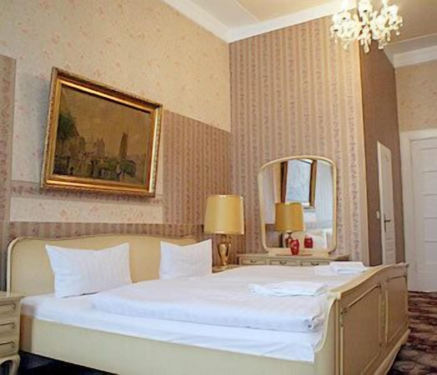 A hotel room with a bed, a nightstand, a lamp, a mirror, and a painting on the wall.