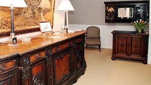 Una habitación con un aparador de madera, dos lámparas, una silla y un cuadro grande en la pared.