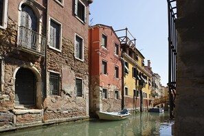 A narrow canal with buildings on either side, a boat docked in the water, and a bridge in the background. - B&B Al Palazzetto (Venice)
