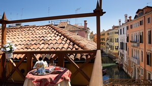 Un balcón con mesa lista para comer, con vista a un canal y edificios.