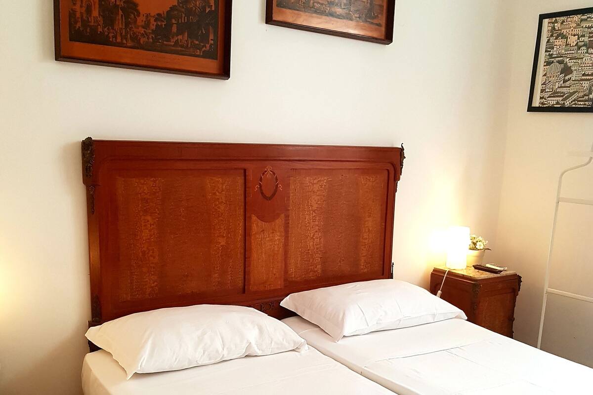 A double bed with white linens, a wooden headboard, and two framed pictures on the wall.