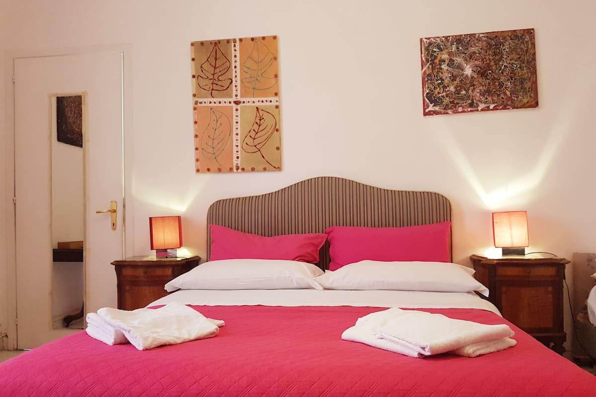 A bed with a red quilt, two white pillows, and two pink pillows. There are two bedside tables with lamps.