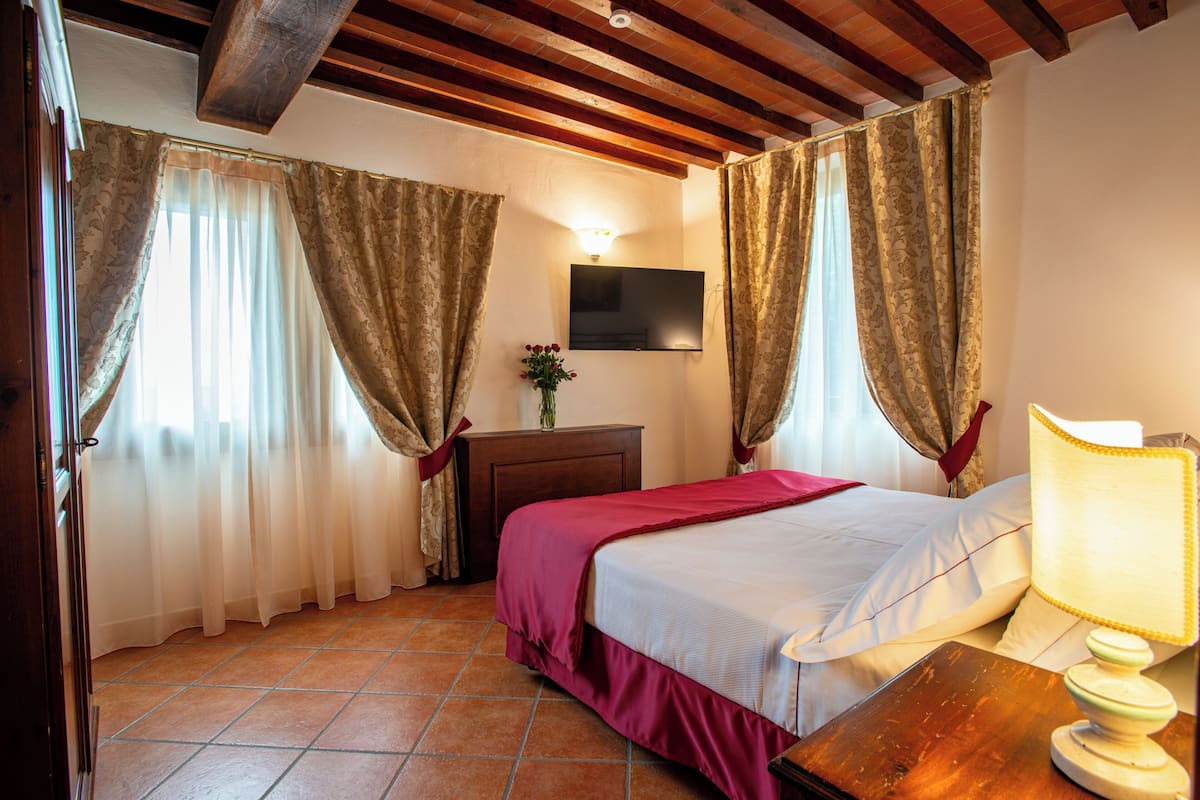 A hotel room with a bed, curtains, a TV, a nightstand, and a lamp.