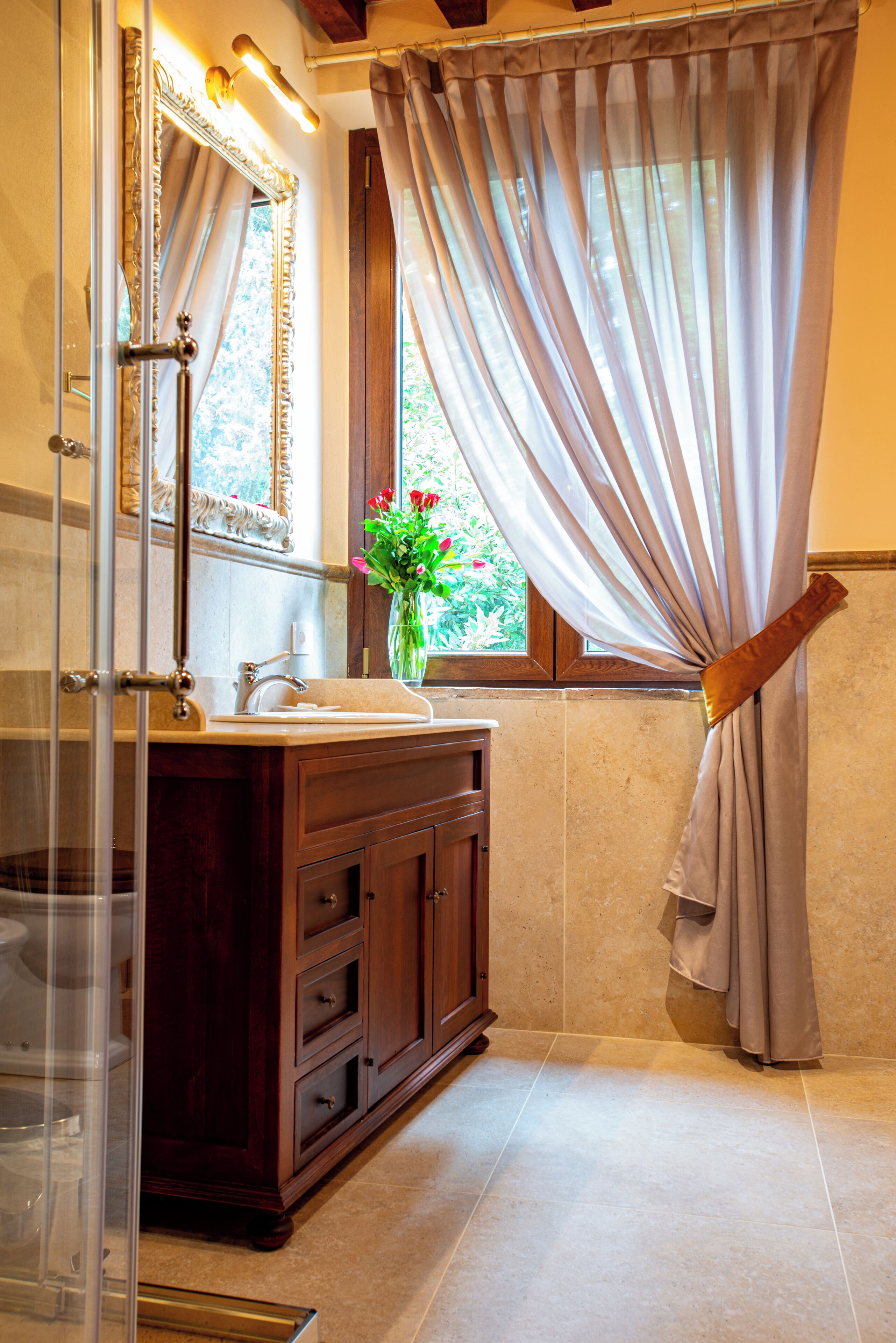 A bathroom with a vanity, mirror, and window with curtains.