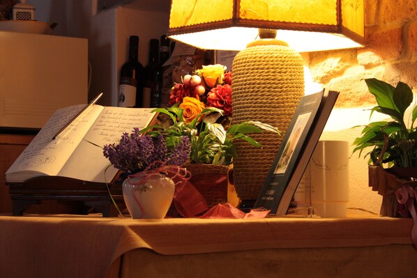 A table with an open book, a lamp, and various decorative items including flowers and a vase. - Hotel Torciano Vecchio Asilo (San Gimignano)