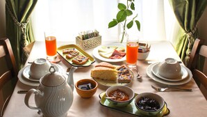 Una mesa de desayuno con té, jugo, sándwiches y un jarrón de flores.