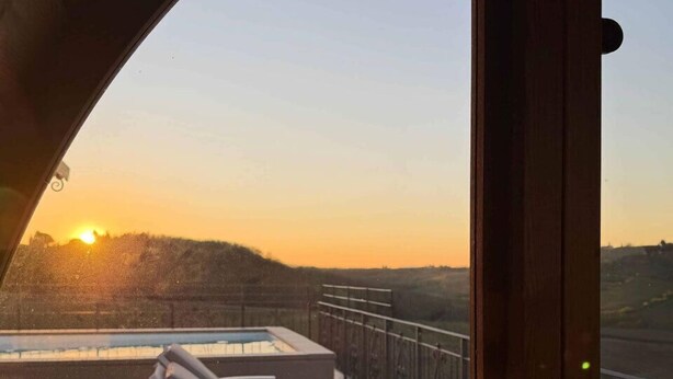 Un balcón con vistas a la puesta de sol, una piscina y un contenedor metálico con rocas.