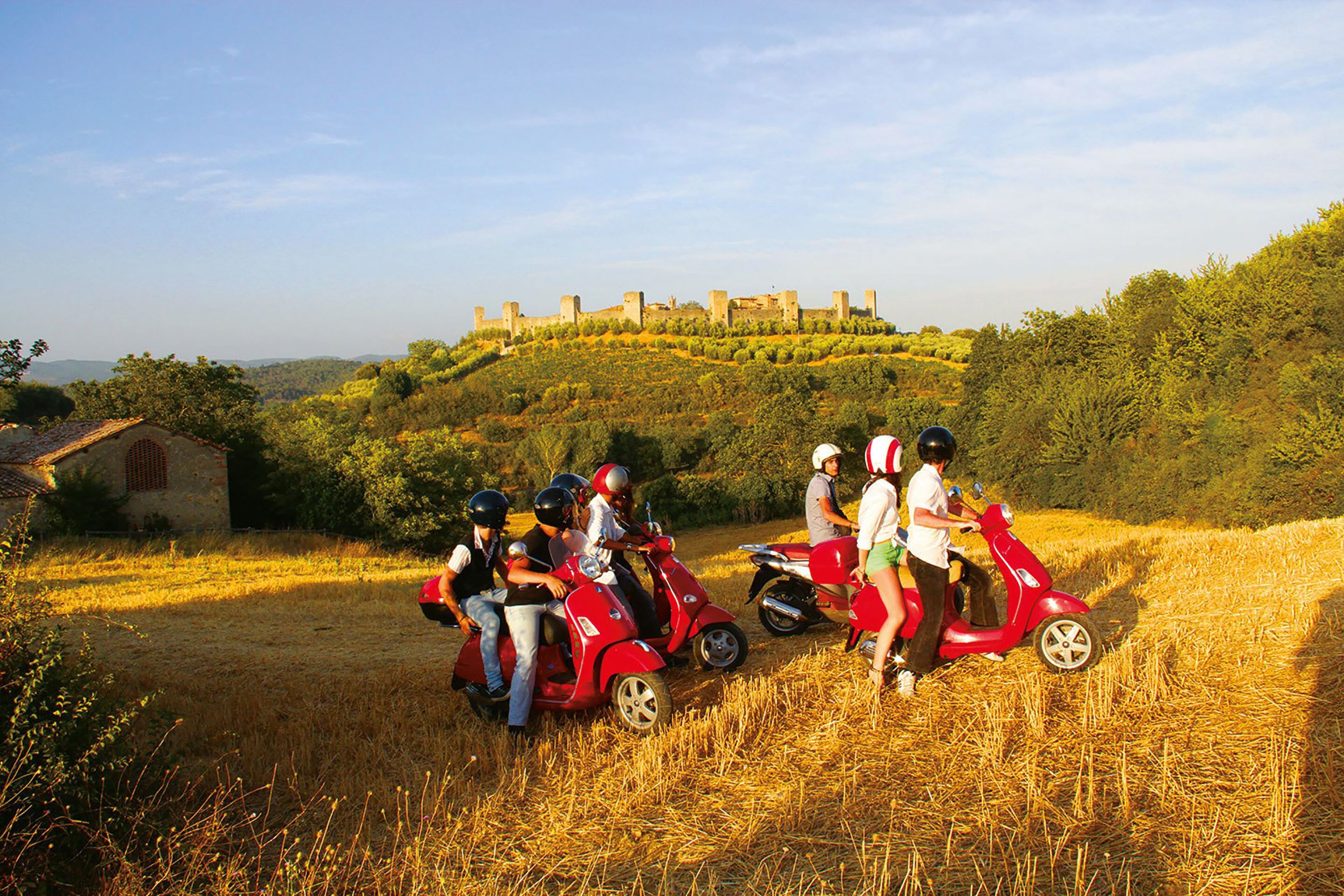 Un groupe de personnes sur des scooters, dans un cadre rural, avec un château en arrière-plan.
