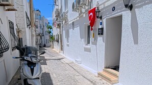 A narrow cobblestone street with a parked scooter, white buildings, and a red flag. - Merhaba Pansiyon (Bodrum)