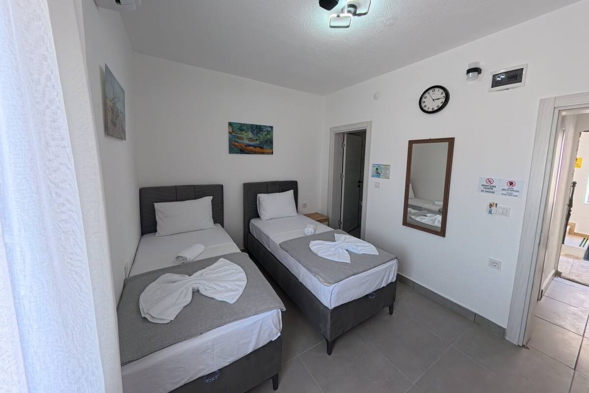 A hotel room with two beds, a clock, a mirror, and a door.