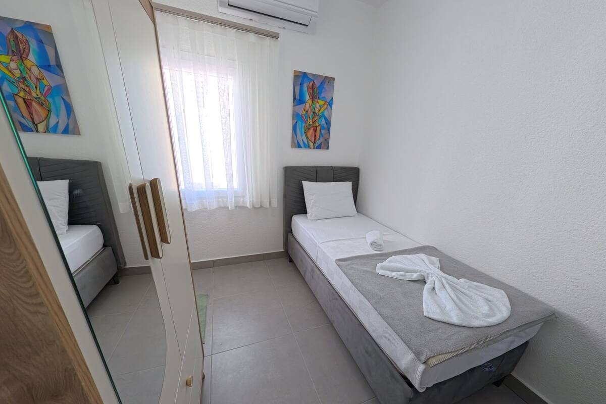 A bedroom with a bed, a window with curtains, a painting on the wall, and a towel on the bed.