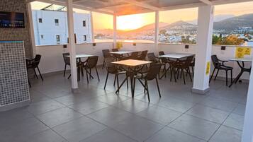 A rooftop terrace with tables and chairs, a view of a cityscape and mountains, and a tiled floor.