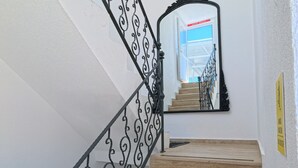 A staircase with ornate black railings, wooden steps, and a mirror reflecting a room with a blue sky view. - Merhaba Pansiyon (Bodrum)