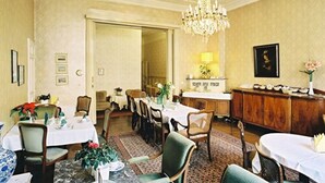 A formal dining room with multiple tables and chairs, a chandelier, and a wooden cabinet. - Hotel-Pension Funk (Berlin)