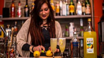 Un bar con un cantinero preparando bebidas, una variedad de botellas y una botella grande de jugo de limón sobre la barra.