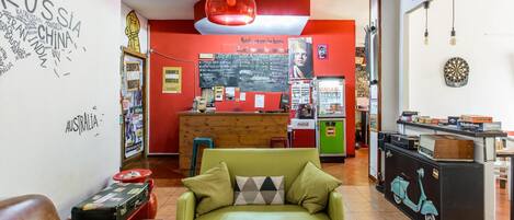 Un hall de hotel acogedor con un sofá verde, un mostrador de recepción de madera y un dardo en la pared.