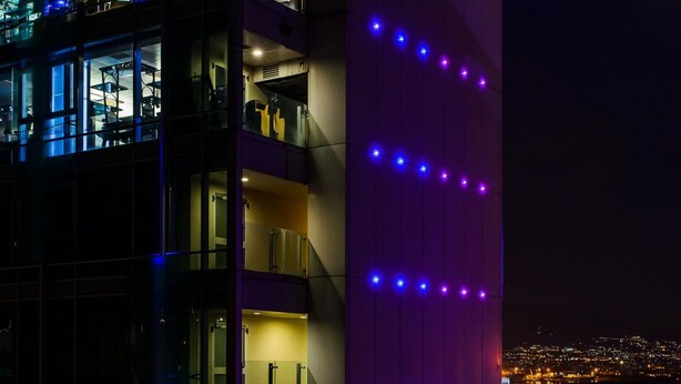 Ein mehrstöckiges Gebäude mit beleuchteten Fenstern und einer violett beleuchteten Wand.