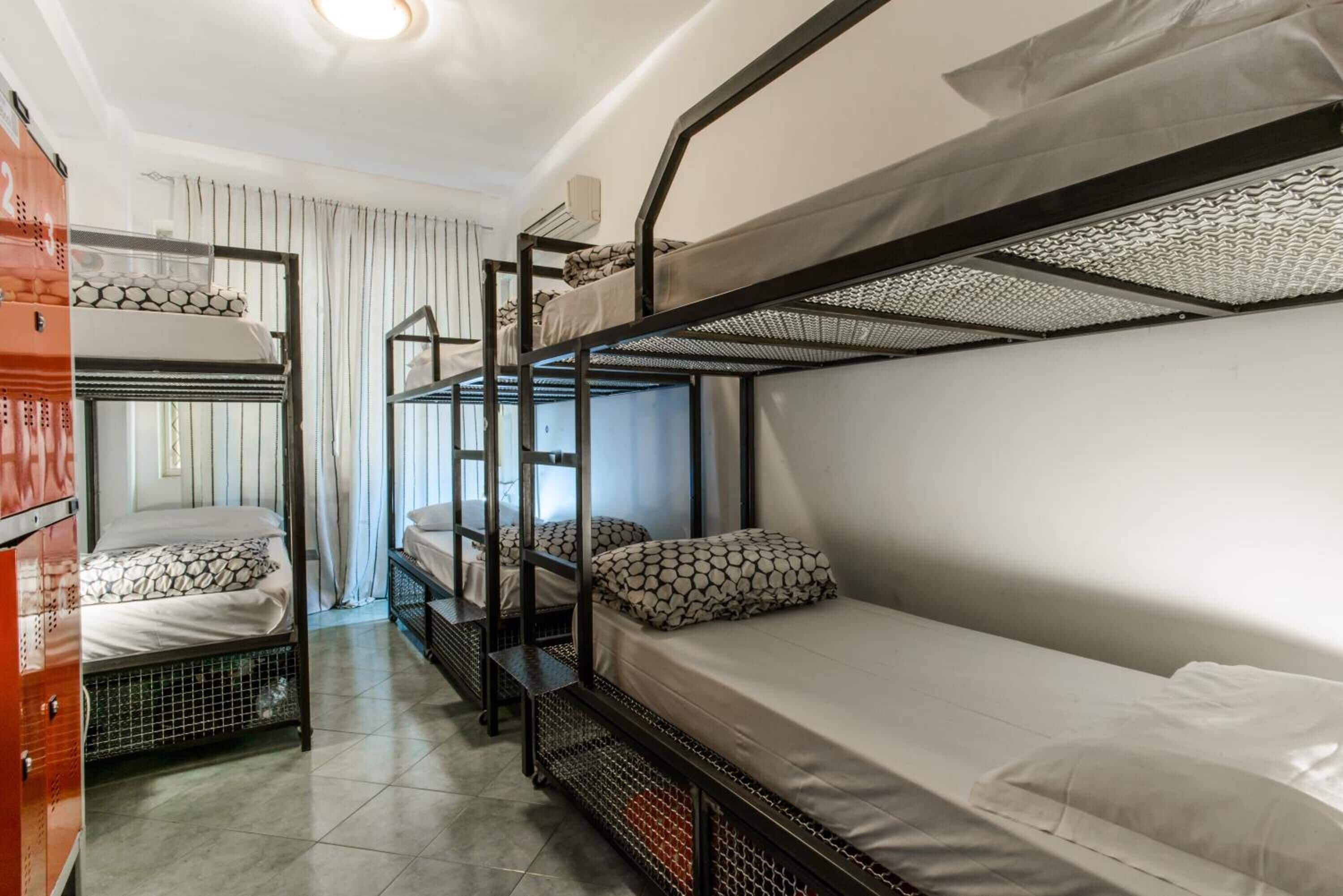 A dormitory room with bunk beds, a window with curtains, and a radiator.