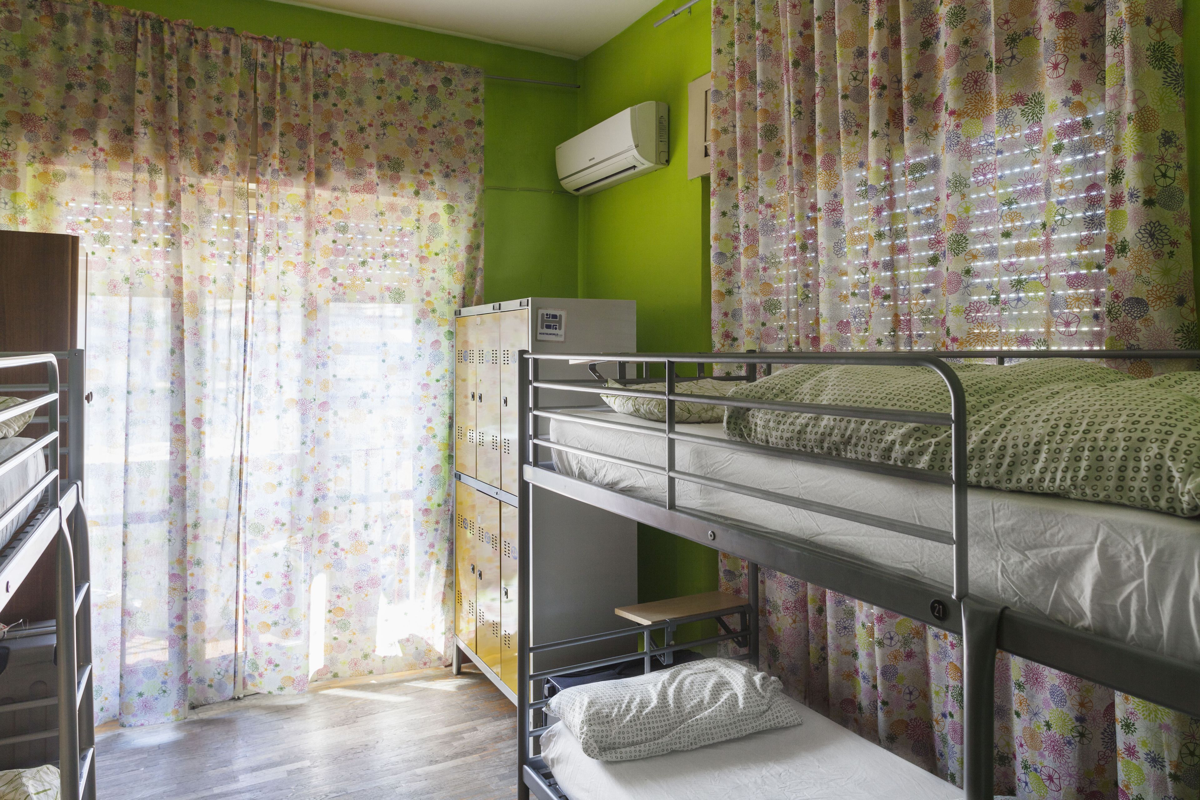 Une chambre avec un lit superposé, un mur vert, des rideaux à motifs floraux et une fenêtre avec des stores.