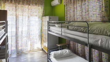 Une chambre avec un lit superposé, un mur vert, des rideaux à motifs floraux et une fenêtre avec des stores.