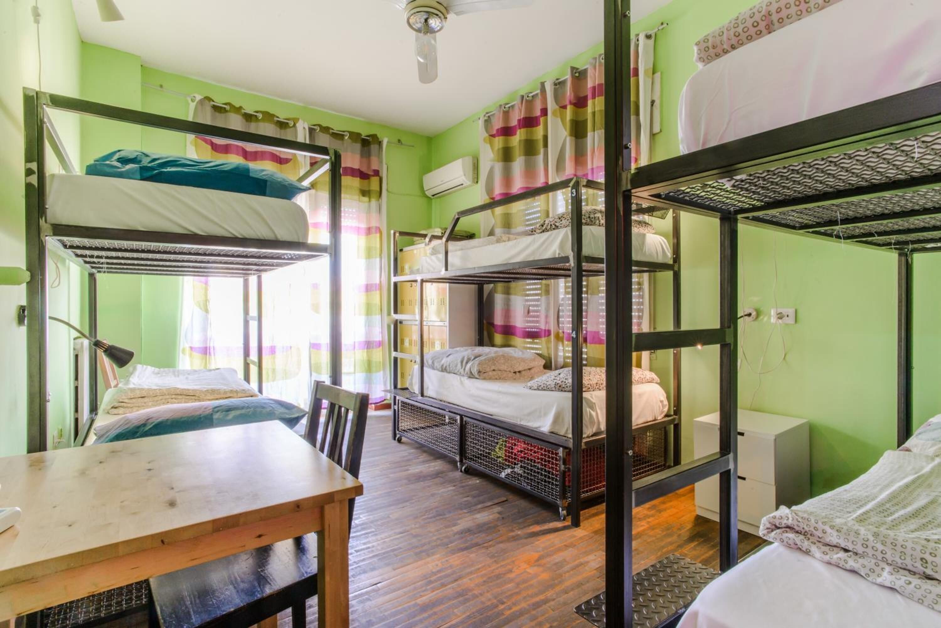 A dormitory room with bunk beds, a wooden desk, and a chair.