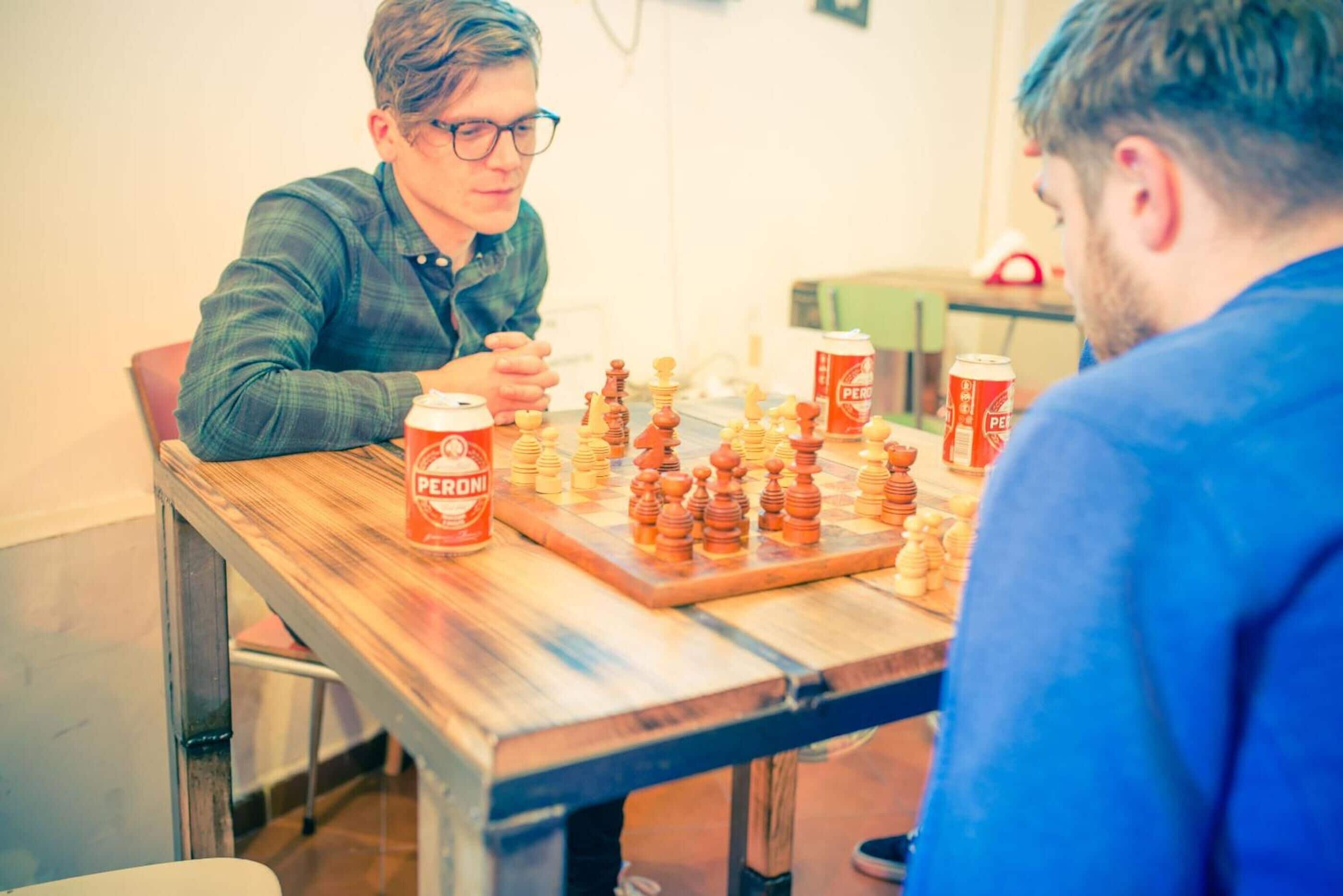 Dos personas jugando ajedrez en una mesa de madera con una lata de cerveza Peroni.