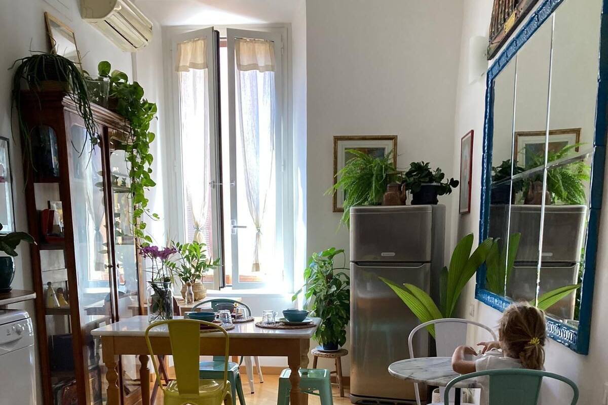 A cozy kitchen with wooden flooring, a dining table with chairs, a refrigerator, and potted plants.