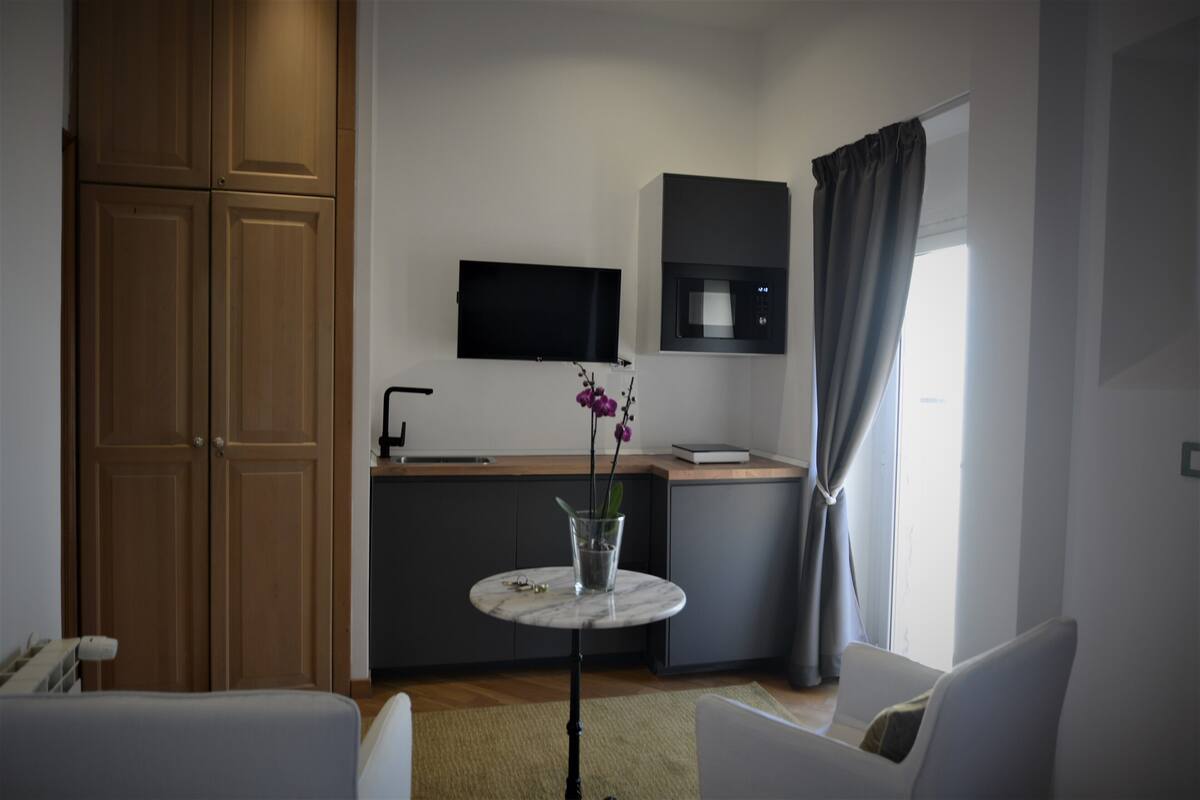 A modern, compact living space with a kitchen area, a dining table with a vase of flowers, and a seating area with two chairs.